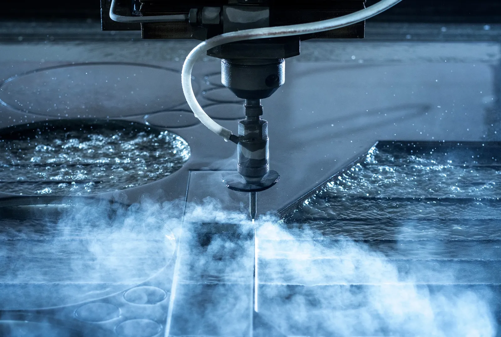 High-pressure nozzle head cutting a metal sheet, surrounded by water mist